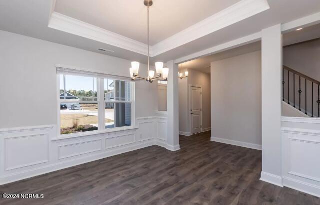 unfurnished dining area with dark hardwood / wood-style flooring, crown molding, a raised ceiling, and an inviting chandelier