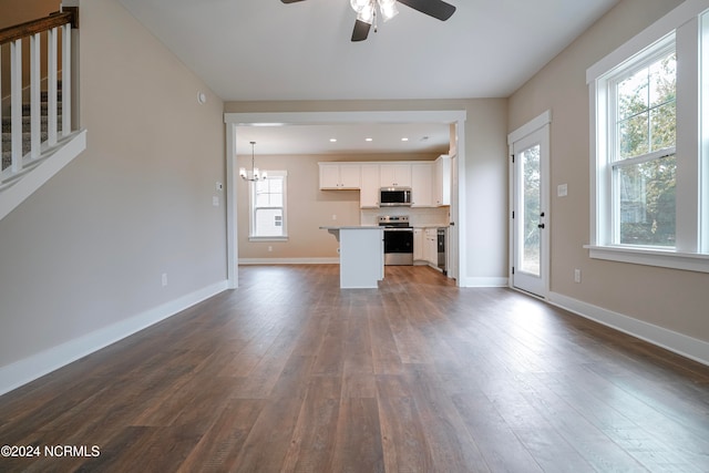 unfurnished living room featuring dark wood-type flooring, ceiling fan with notable chandelier, and a healthy amount of sunlight