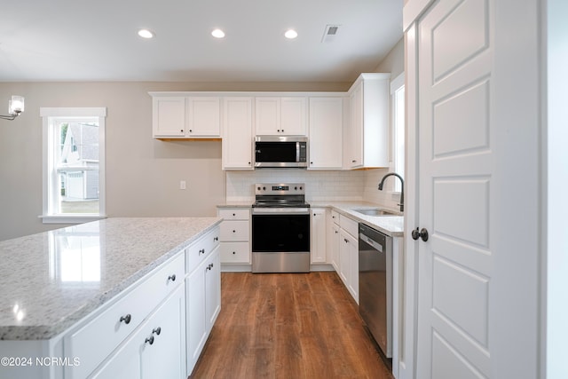 kitchen with light stone counters, appliances with stainless steel finishes, white cabinetry, dark wood-type flooring, and sink