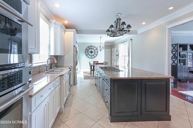 kitchen with light stone counters, crown molding, white cabinetry, a center island, and sink