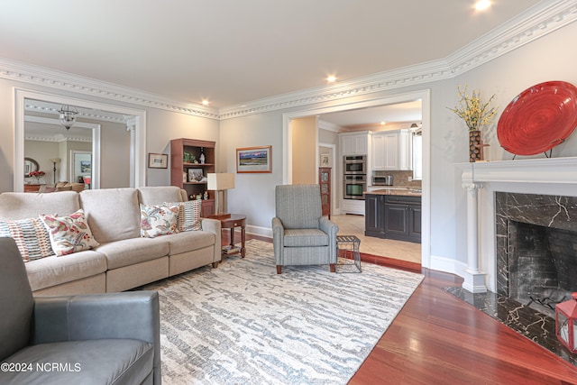 living room with a high end fireplace, ornamental molding, and light hardwood / wood-style floors