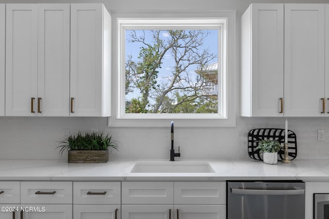 kitchen with light stone countertops, dishwasher, white cabinets, and sink