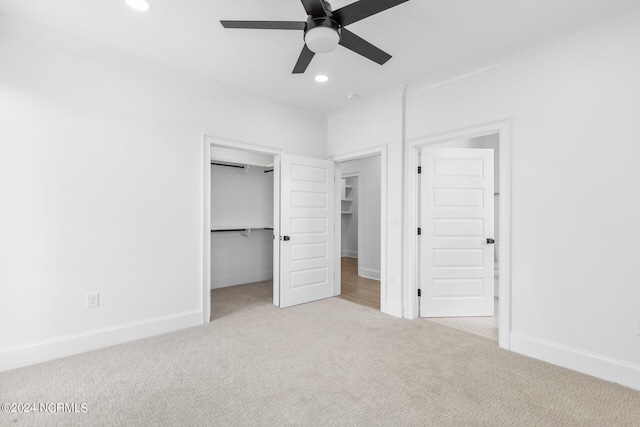 unfurnished bedroom with a walk in closet, ceiling fan, a closet, and light carpet