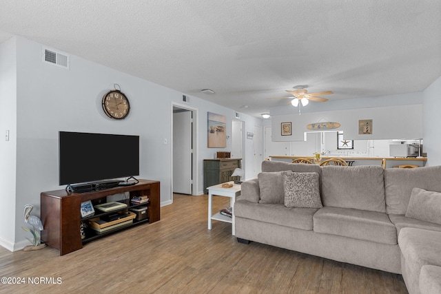 living room featuring a textured ceiling, wood-type flooring, and ceiling fan