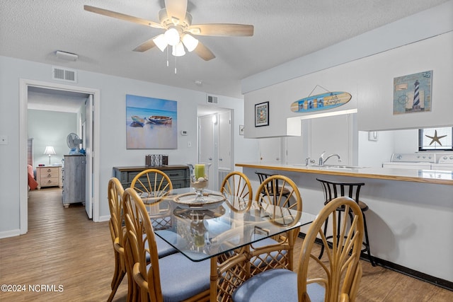 dining room featuring ceiling fan, washing machine and clothes dryer, a textured ceiling, and light hardwood / wood-style flooring