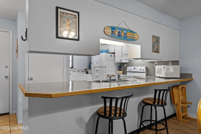 kitchen with washer / clothes dryer, kitchen peninsula, hardwood / wood-style flooring, white cabinets, and white appliances