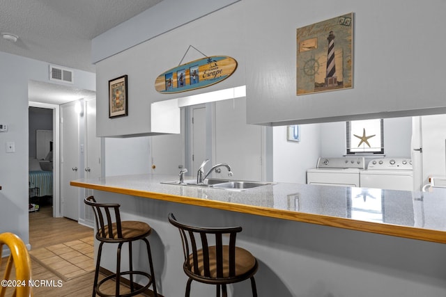 kitchen featuring hardwood / wood-style flooring, sink, separate washer and dryer, a breakfast bar area, and white cabinetry