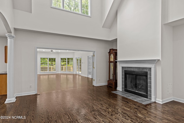 unfurnished living room with a tile fireplace, a towering ceiling, dark wood-type flooring, and a healthy amount of sunlight