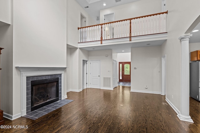 unfurnished living room with a tile fireplace, a high ceiling, decorative columns, and dark wood-type flooring