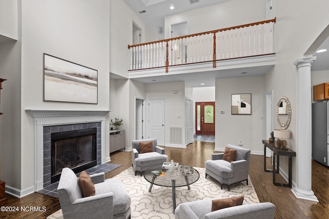 living room featuring decorative columns, a tile fireplace, a towering ceiling, and dark wood-type flooring