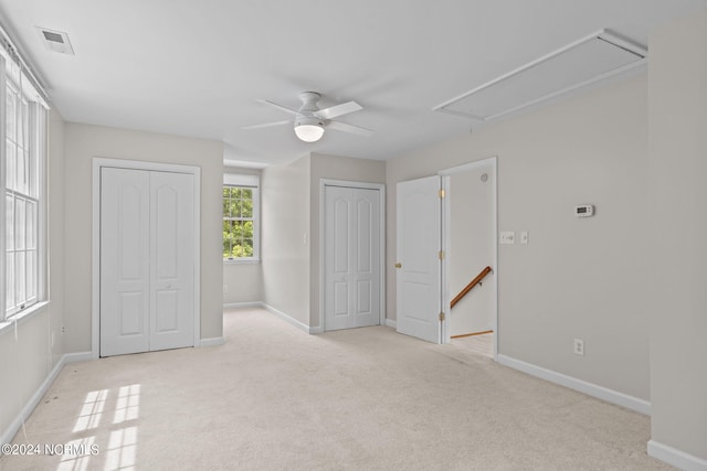 unfurnished bedroom with two closets, light colored carpet, and ceiling fan