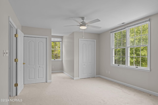 unfurnished bedroom featuring ceiling fan, light carpet, and two closets