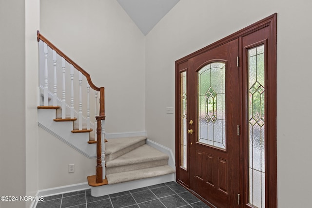 foyer entrance with dark tile patterned flooring and lofted ceiling