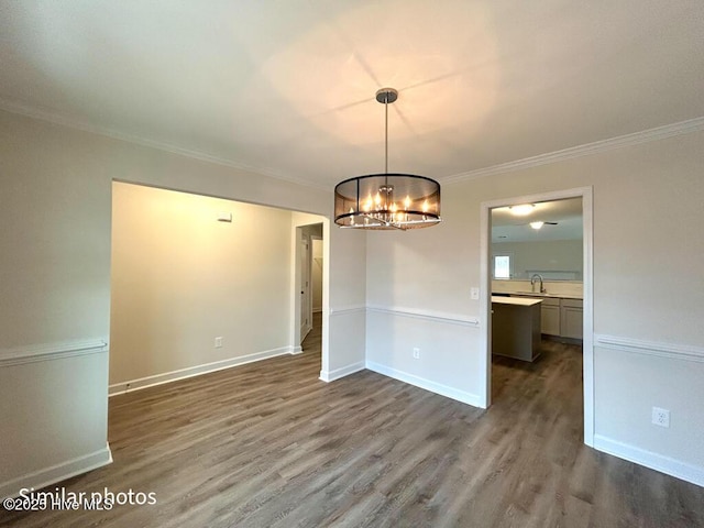 unfurnished dining area with sink, wood-type flooring, crown molding, and a notable chandelier