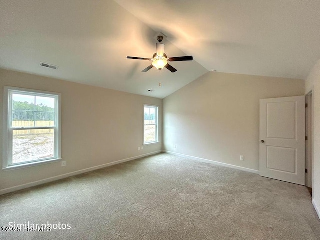 empty room featuring a healthy amount of sunlight, lofted ceiling, light colored carpet, and ceiling fan