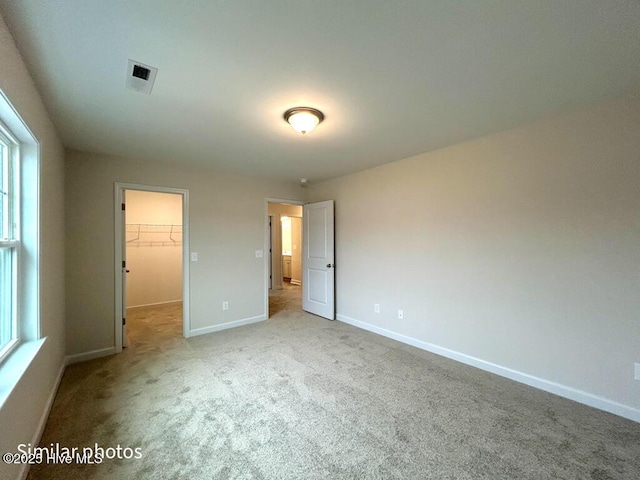 unfurnished bedroom with a spacious closet, a closet, and light colored carpet