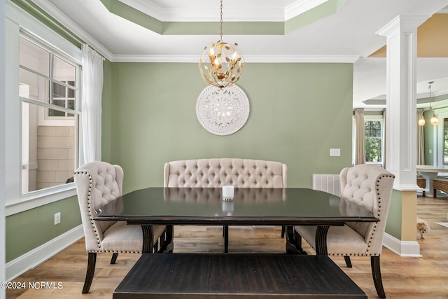 dining space with an inviting chandelier, a raised ceiling, crown molding, hardwood / wood-style flooring, and ornate columns