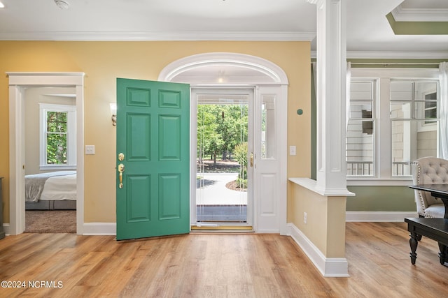 entrance foyer featuring decorative columns, a wealth of natural light, ornamental molding, and light wood-type flooring