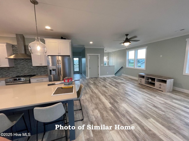 kitchen featuring appliances with stainless steel finishes, light countertops, white cabinetry, and wall chimney exhaust hood