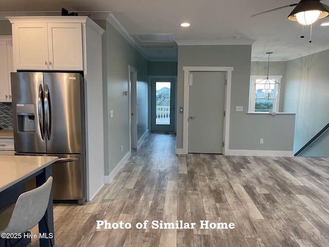 kitchen with stainless steel fridge, ornamental molding, hanging light fixtures, light countertops, and white cabinetry