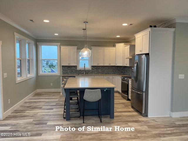 kitchen with hanging light fixtures, appliances with stainless steel finishes, a kitchen island, and white cabinets