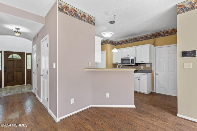 kitchen with dark wood-style floors, a peninsula, stainless steel microwave, and white cabinetry