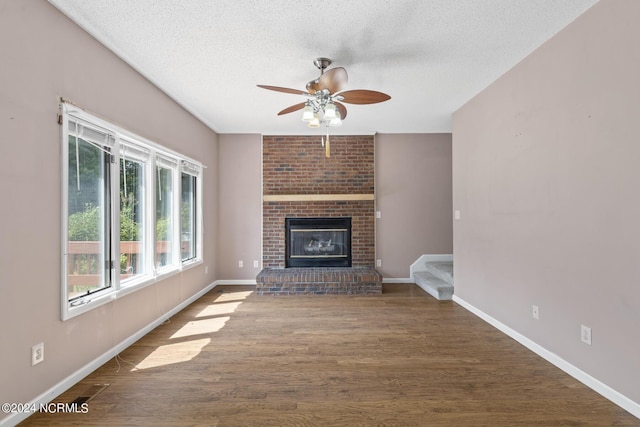 unfurnished living room with baseboards, ceiling fan, dark wood-style flooring, a textured ceiling, and a fireplace