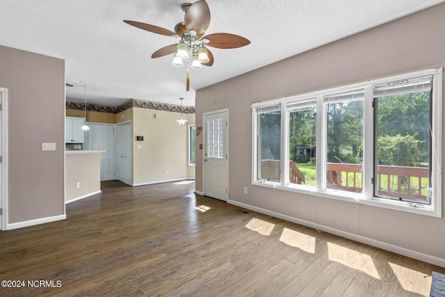 unfurnished living room with a textured ceiling, dark wood finished floors, a ceiling fan, and baseboards