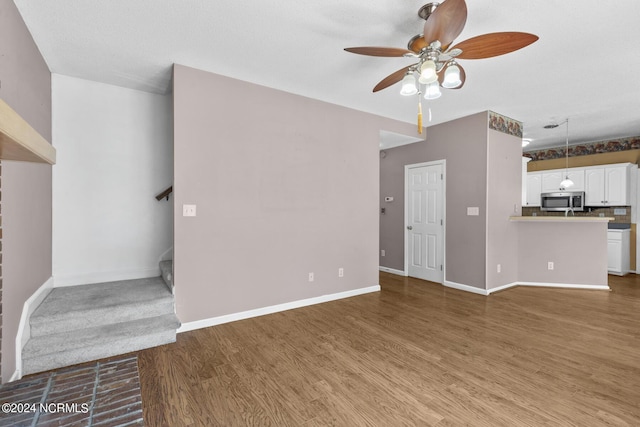 unfurnished living room with a ceiling fan, stairs, baseboards, and wood finished floors