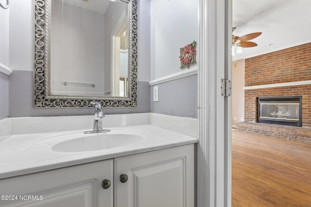 bathroom with a brick fireplace, ceiling fan, wood finished floors, and vanity