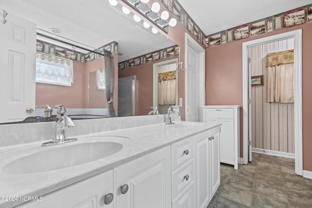 full bathroom featuring a textured ceiling, double vanity, a sink, and baseboards