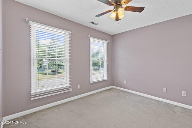 carpeted empty room with a textured ceiling, ceiling fan, visible vents, and baseboards