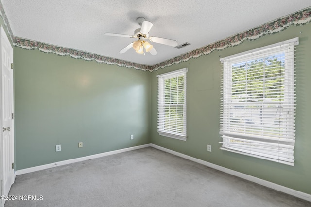 carpeted empty room featuring a textured ceiling, ceiling fan, visible vents, and baseboards