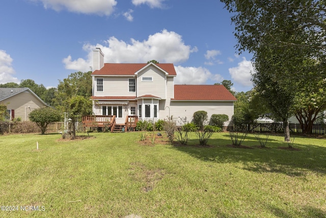 back of house featuring a chimney, fence, a deck, and a lawn