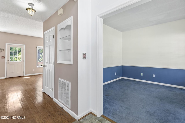 corridor featuring baseboards, visible vents, dark wood-style floors, a textured ceiling, and dark carpet