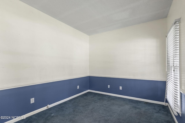 empty room featuring lofted ceiling, a textured ceiling, dark carpet, and baseboards