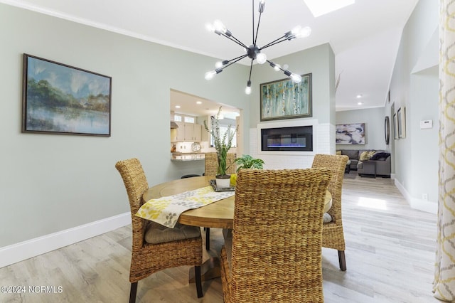 dining room with a glass covered fireplace, light wood-style flooring, a notable chandelier, and baseboards