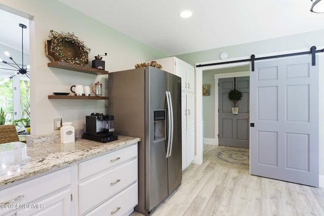 kitchen with light wood-style floors, white cabinets, a barn door, light stone counters, and stainless steel fridge