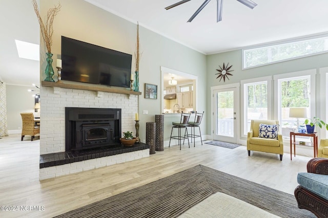 living room featuring baseboards, ornamental molding, ceiling fan, wood finished floors, and a skylight