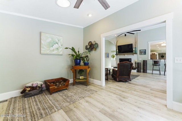 sitting room with baseboards, a brick fireplace, ornamental molding, a ceiling fan, and wood finished floors