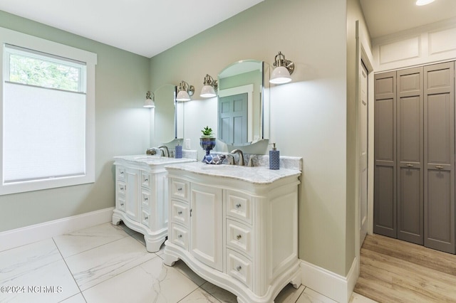 full bathroom with marble finish floor, double vanity, baseboards, and a sink