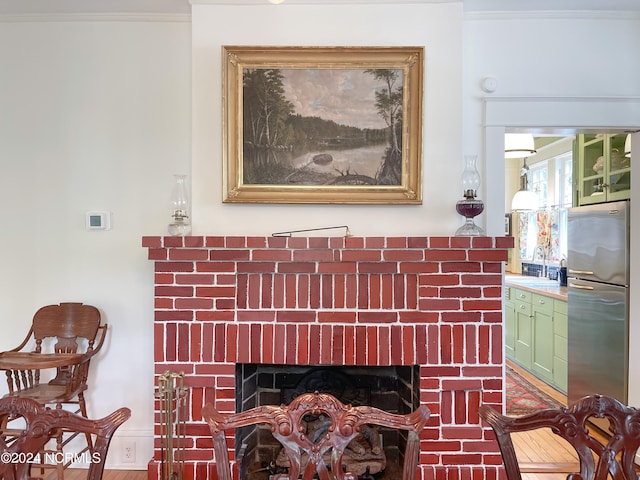 details featuring crown molding, stainless steel fridge, a brick fireplace, wood-type flooring, and sink