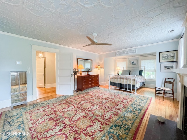 bedroom with ceiling fan, a textured ceiling, ornamental molding, and wood-type flooring