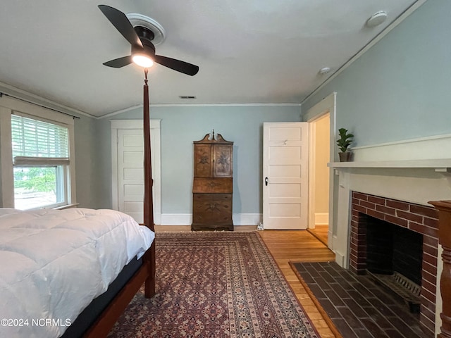 bedroom with crown molding, ceiling fan, wood-type flooring, and a brick fireplace