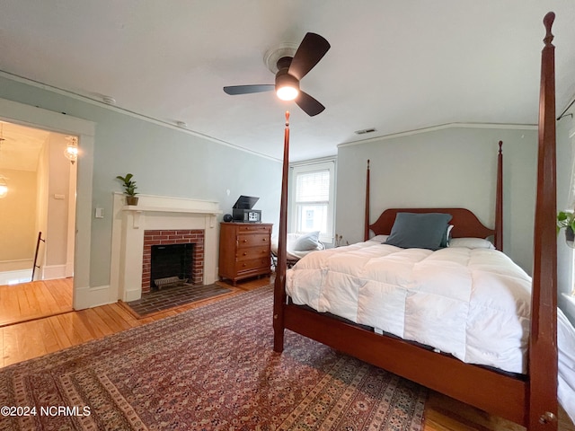 bedroom with ceiling fan, hardwood / wood-style floors, ornamental molding, and a brick fireplace