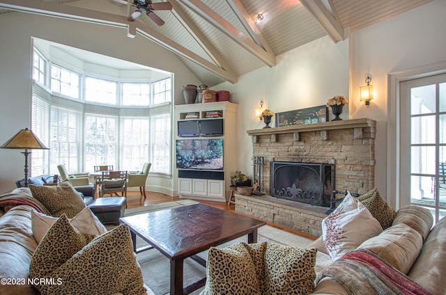 living room featuring high vaulted ceiling, a stone fireplace, beam ceiling, and a healthy amount of sunlight