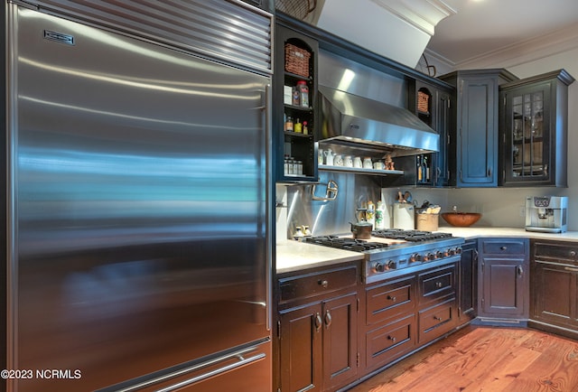 kitchen with wall chimney exhaust hood, wood-type flooring, dark brown cabinets, and stainless steel appliances