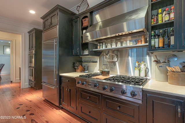 kitchen with ornamental molding, light hardwood / wood-style flooring, appliances with stainless steel finishes, wall chimney exhaust hood, and dark brown cabinetry