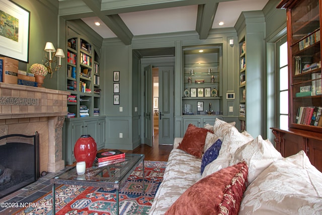 living room with dark wood-type flooring, built in shelves, a tile fireplace, beam ceiling, and coffered ceiling