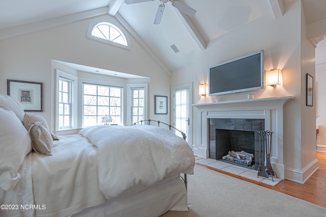 bedroom featuring ceiling fan, beamed ceiling, multiple windows, a fireplace, and wood-type flooring